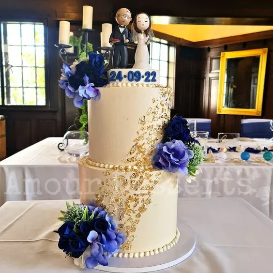 Two-tier custom cake with blue florals, gold leaf and couple toppers